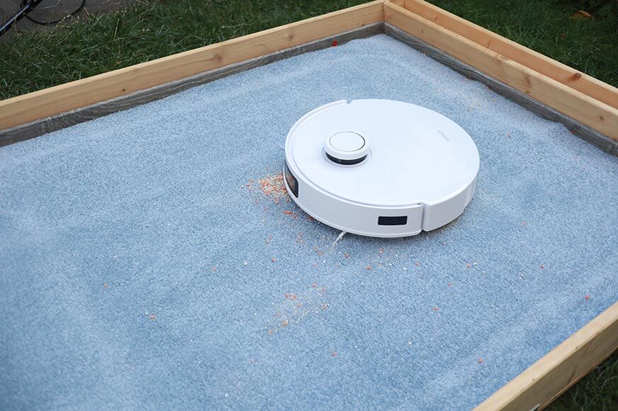 ECOVACS DEEBOT T10 reinigt im Test Haferflocken auf einem hohen Teppich.